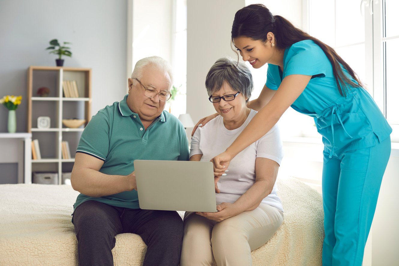 Home Care Nurse Teaching Her Happy Senior Patients to Use Modern Laptop Computer